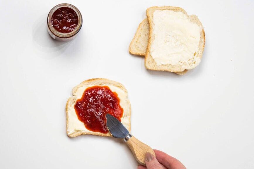 a hand spreading the jam on the sandwich