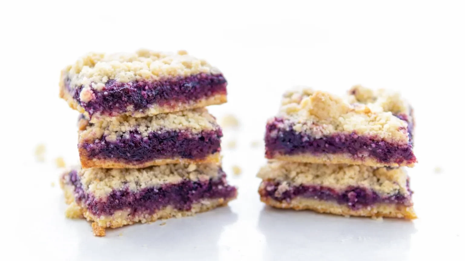 Close-up of blueberry crumb bars showing layers of buttery crust and homemade jam on a white background