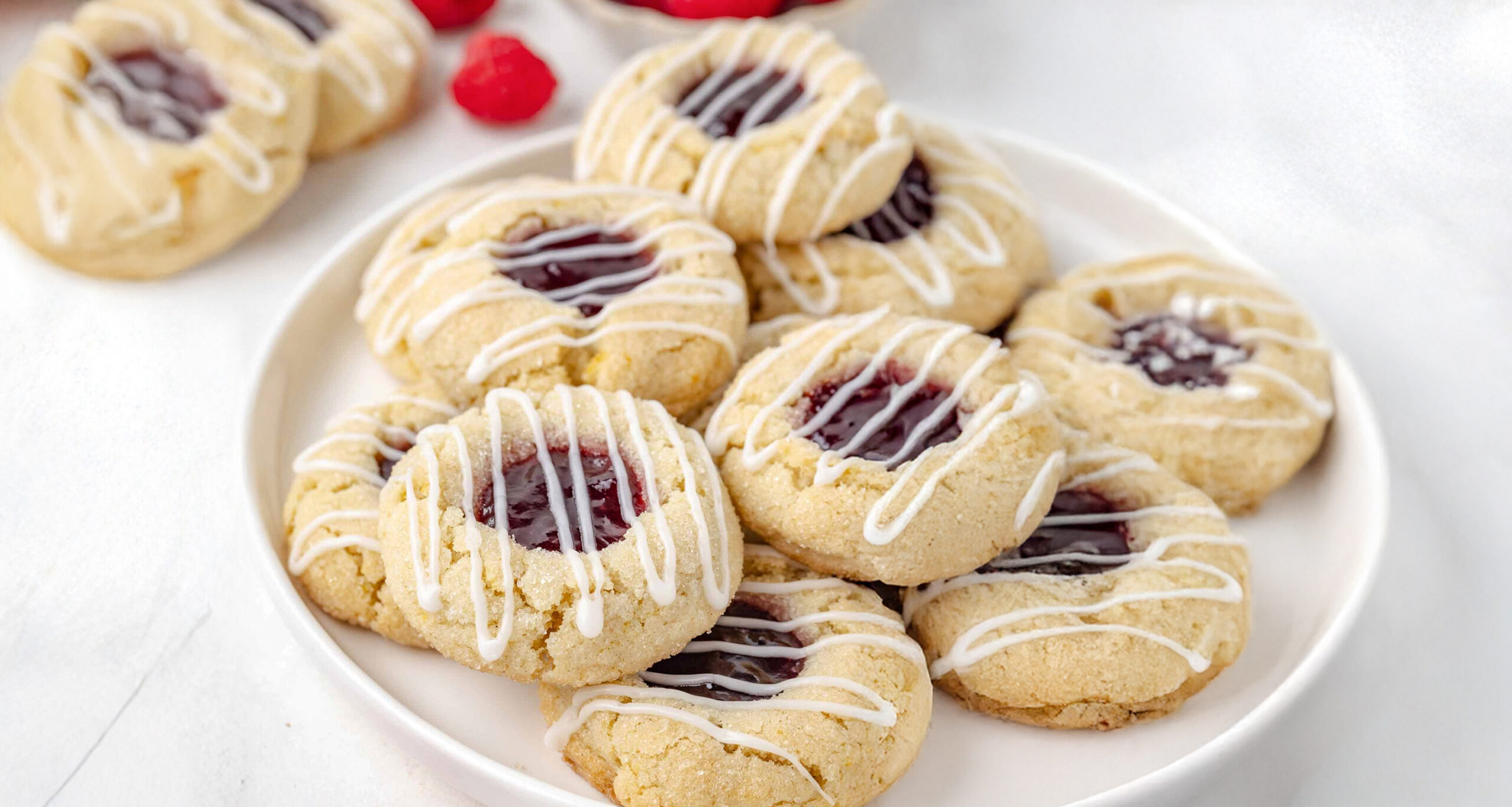 Thumbprint cookies with raspberry jam and white glaze on a white plate